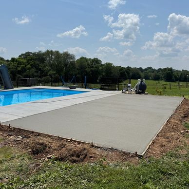 A backyard pool with a slide and a newly poured concrete patio under a partly cloudy sky.