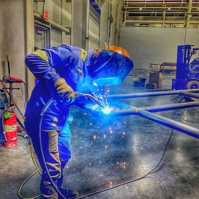 A welder in protective gear welding metal pipes indoors.