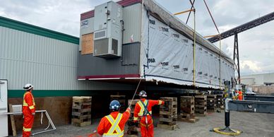 Workers guide heavy machinery for building relocation.