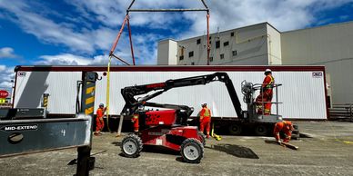 Workers assembling a large white container at a construction site.