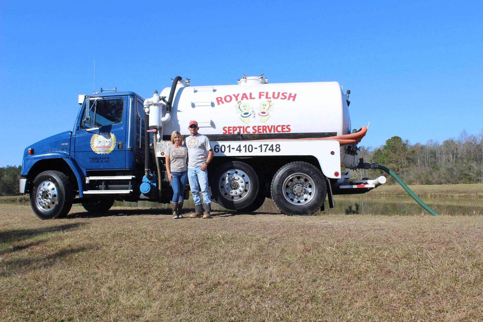 Two people standing in front of a septic services truck.