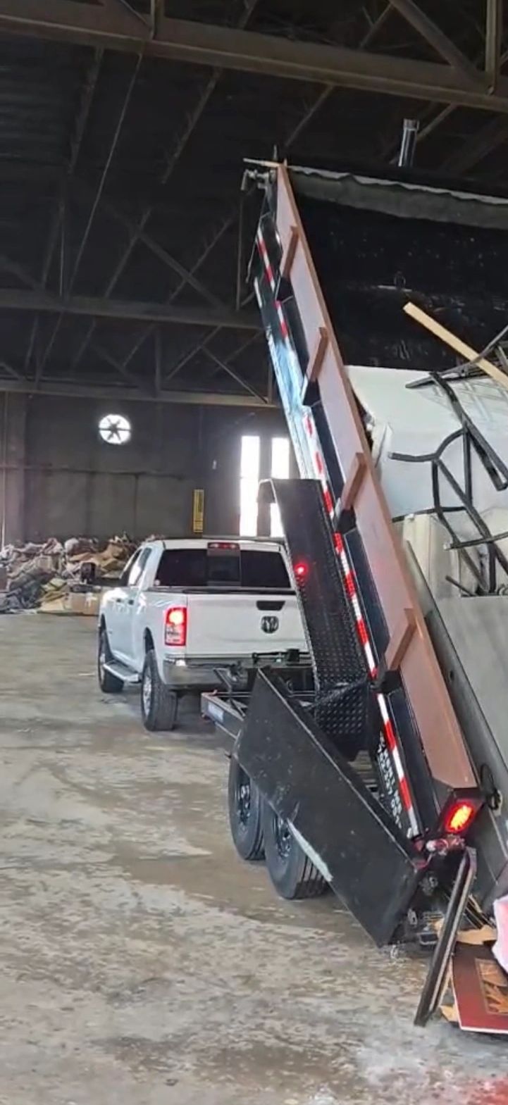A white pickup truck hauling a trailer dumping furniture and mattresses inside a warehouse.
