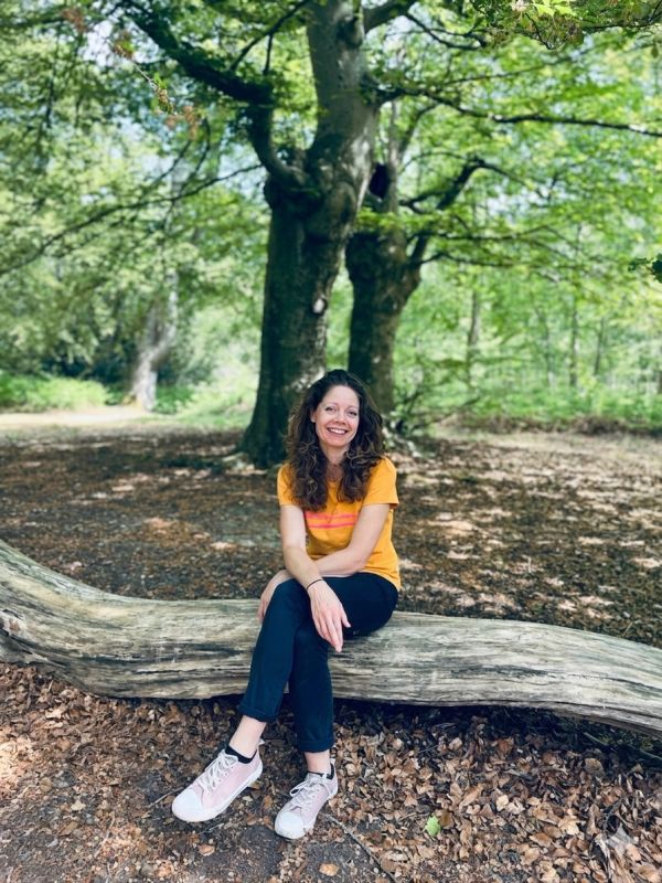 A woman in a yellow shirt sitting on a fallen log in a forest, smiling.