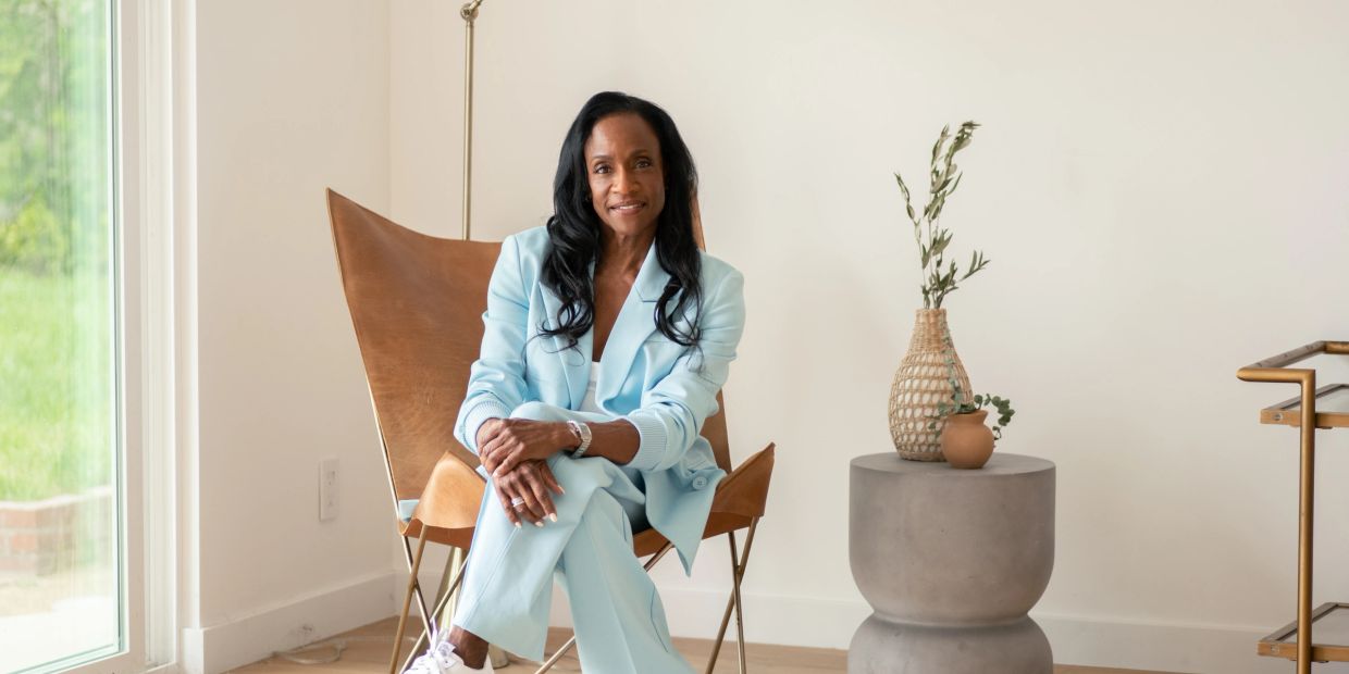 Woman in light blue suit sitting on a chair indoors.