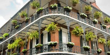 Historic brick building with ornate iron balconies and abundant hanging plants.
