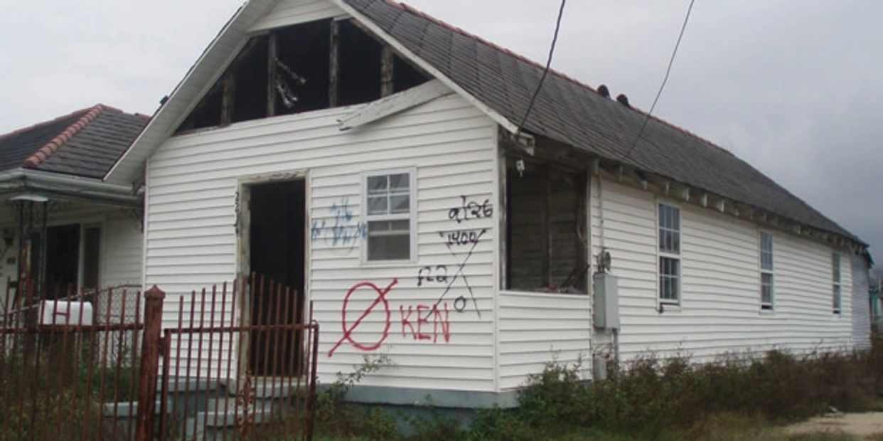 Abandoned house with damaged roof and graffiti on the wall under gray sky.