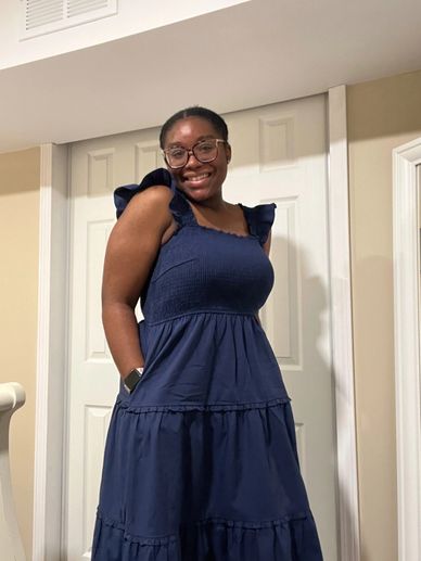 Smiling woman in a navy blue dress with ruffled sleeves standing indoors.