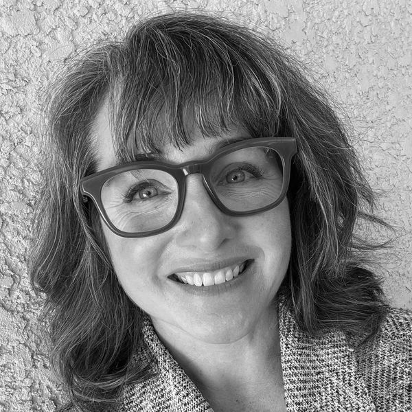 Smiling woman with glasses and wavy hair.