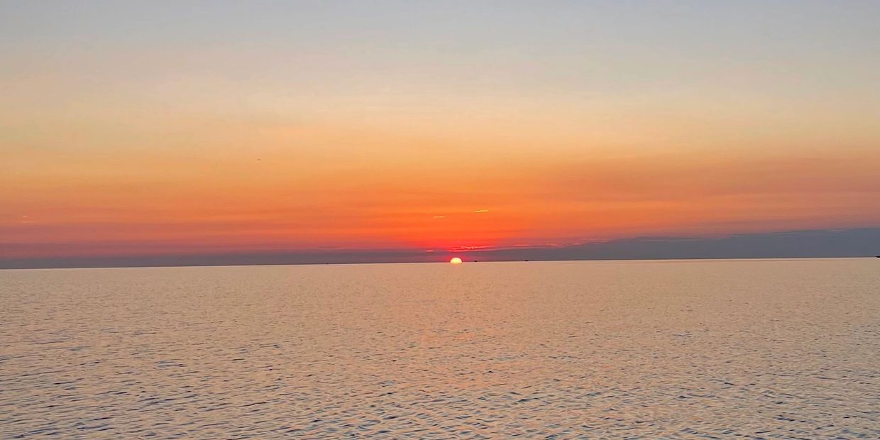 Sun setting over calm ocean waters with a colorful sky.