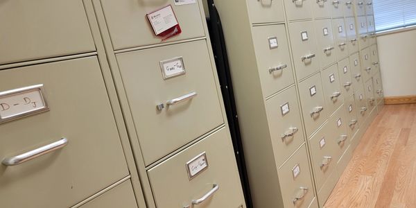 Rows of beige filing cabinets with labeled drawers in an office room.