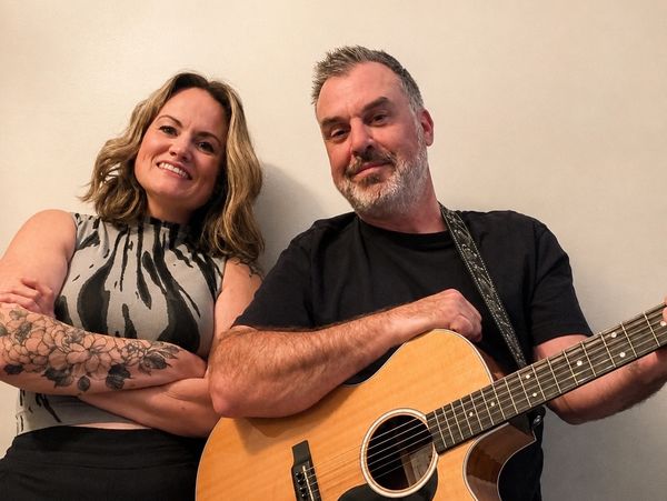 A smiling woman and man with a guitar.