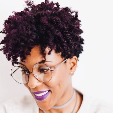 Smiling woman with curly hair and purple lipstick.