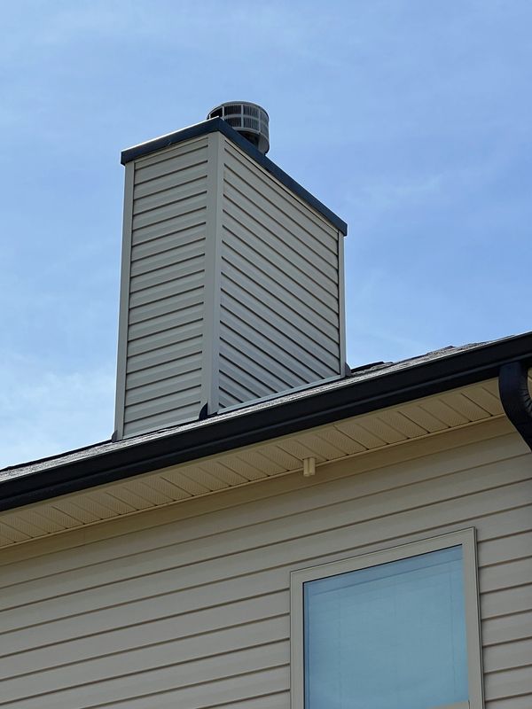 House chimney with beige siding and clear blue sky cleaned by soft wash.
