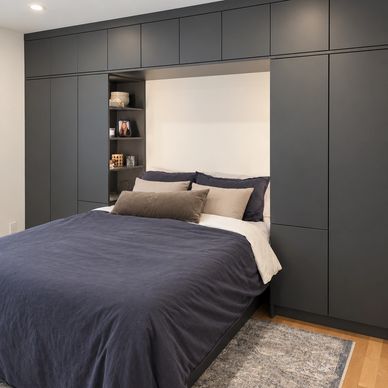 Chambre moderne avec armoires sur mesure gris foncé intégrées autour du lit.