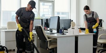 Two janitors cleaning an office with vacuum and disinfectant spray.