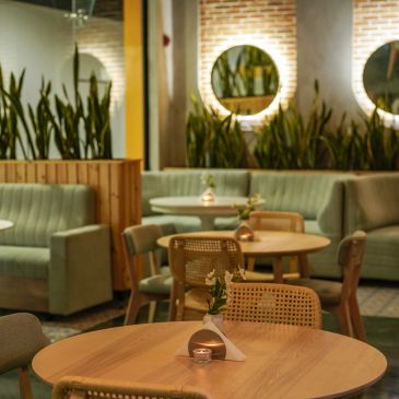 Cozy, modern cafe interior with wooden tables and green plants.