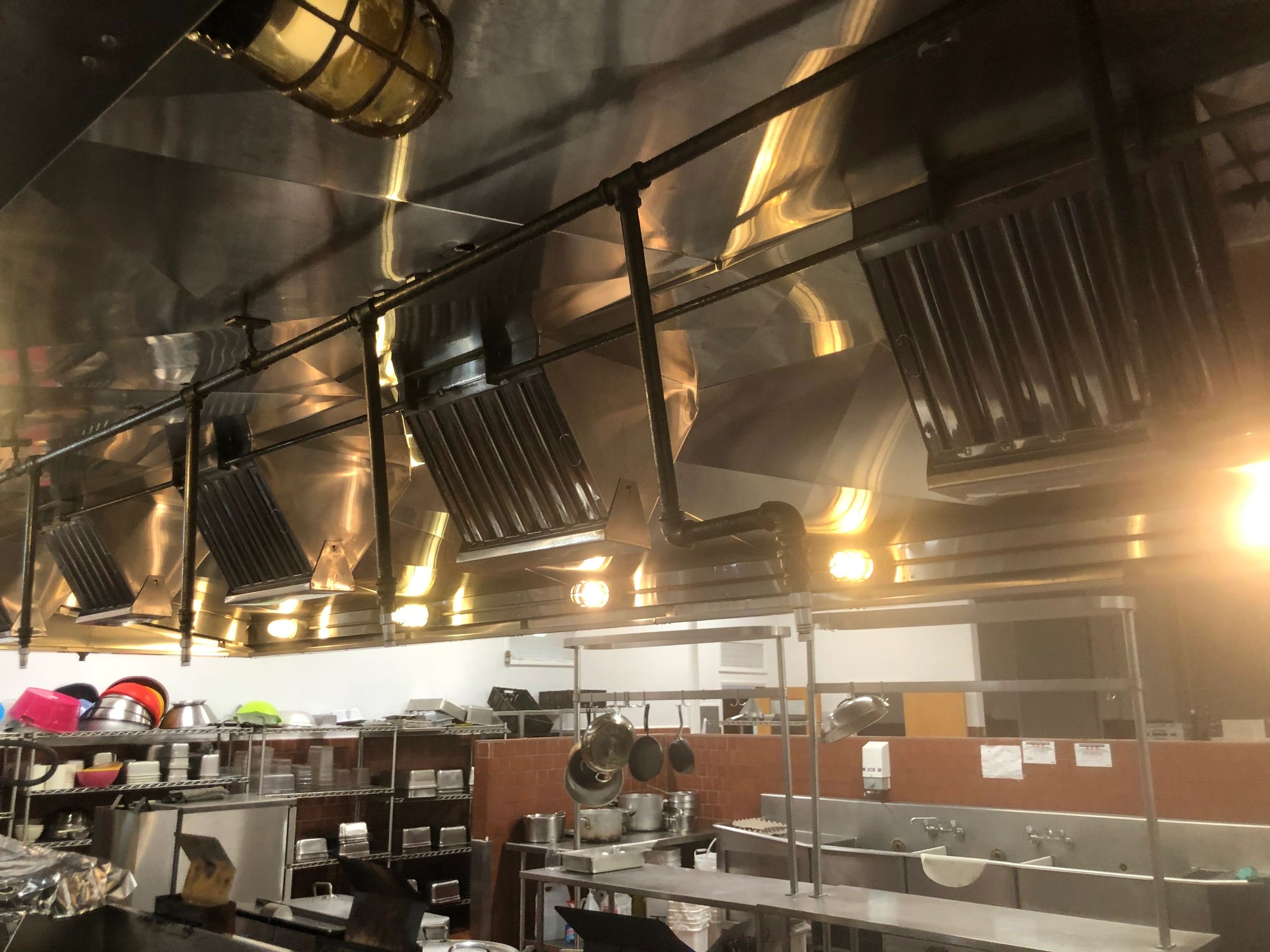 Commercial kitchen with stainless steel ventilation and hanging pots.