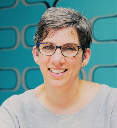 Smiling woman with glasses and short hair in front of a blue patterned background.