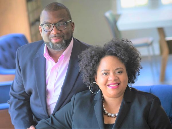 A smiling couple dressed in business attire indoors.