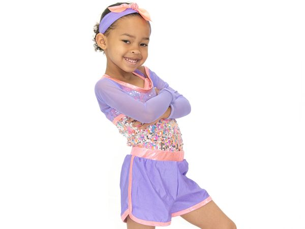 Smiling girl in colorful dance outfit with arms crossed.