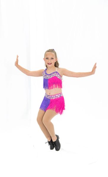 Young girl in vibrant dance costume posing mid-dance against white background.