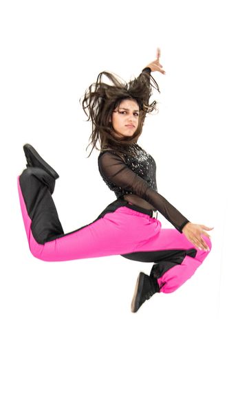 Young woman in vibrant pink and black outfit performing a dynamic jump dance move.