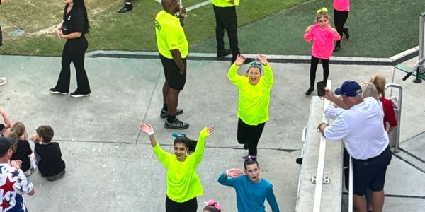 People in bright clothing waving and interacting outdoors at an event.