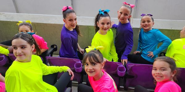 Young girls in colorful outfits posing on purple seats, smiling joyfully.