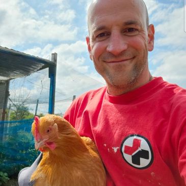 Man smiling with a chicken outdoors.