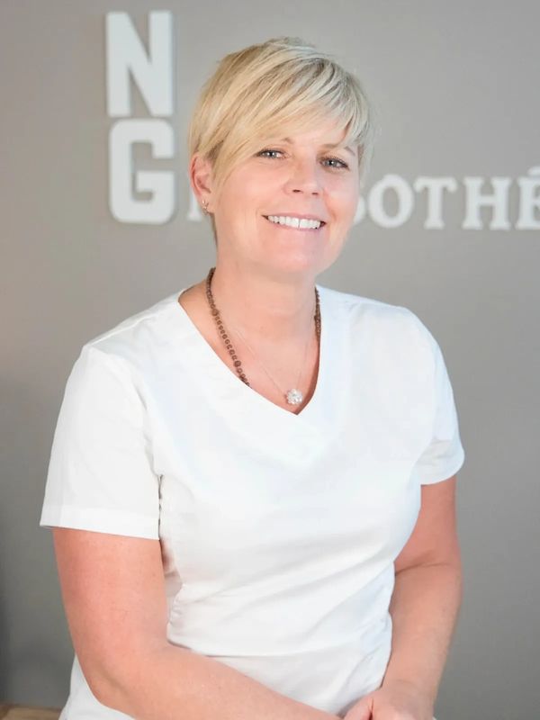 Smiling woman with short blonde hair wearing a white shirt and necklace.