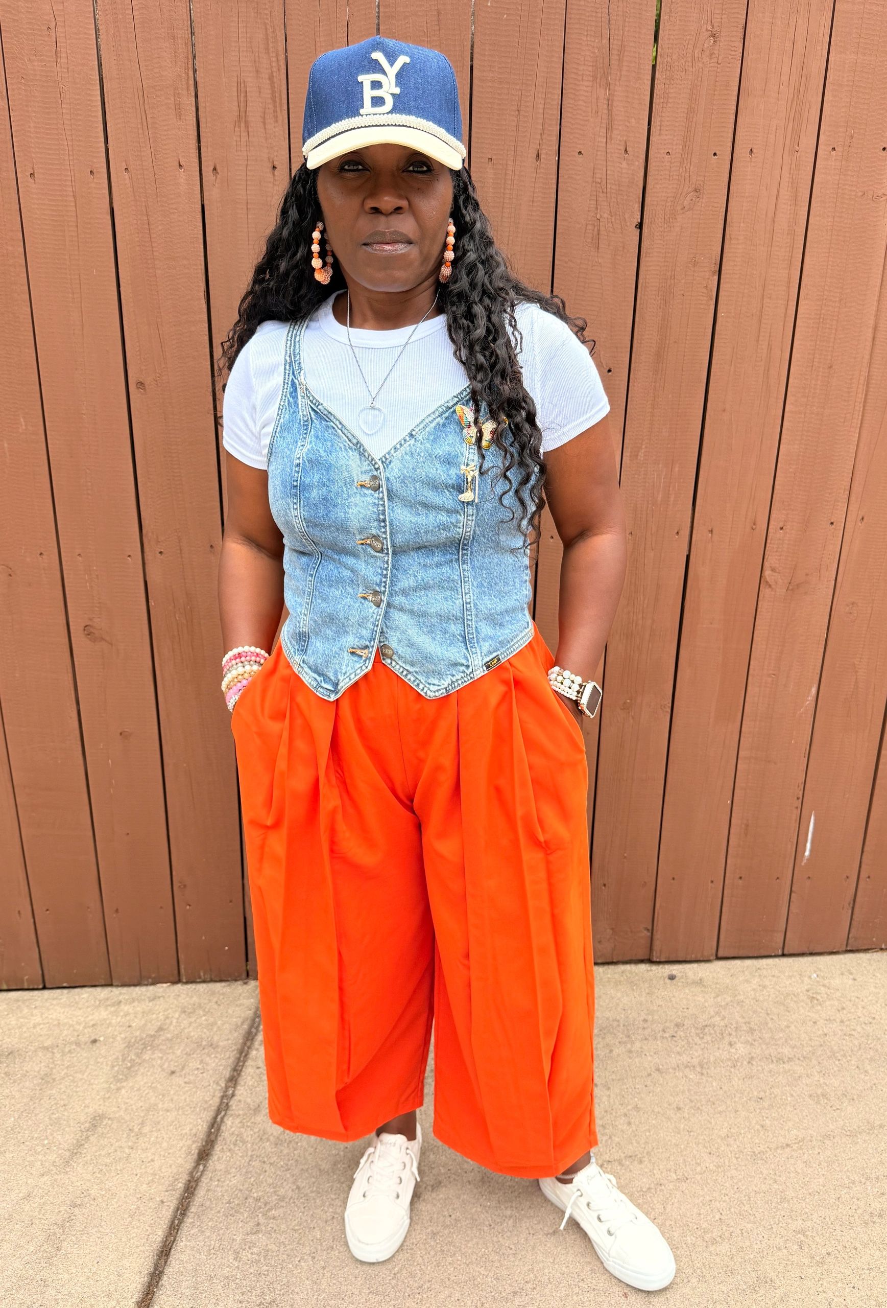 Woman wearing orange pants and a denim vest with a blue cap.