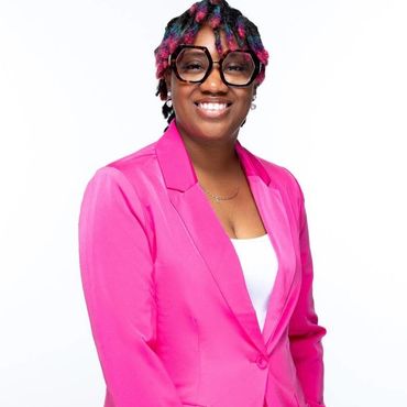 Person smiling wearing a pink blazer and large glasses.
