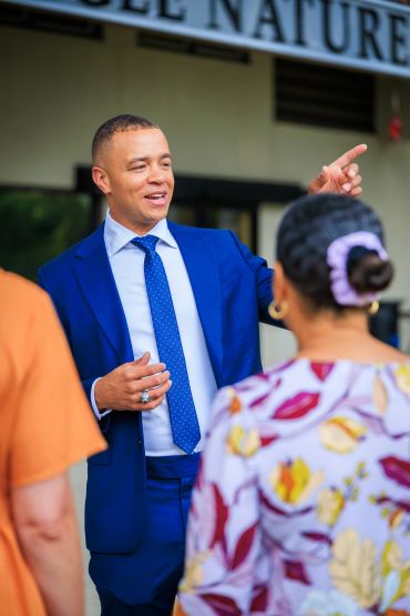 Man in blue suit talking and pointing while two people listen.