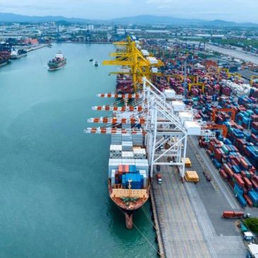 Cargo ship docked at busy container port with cranes.