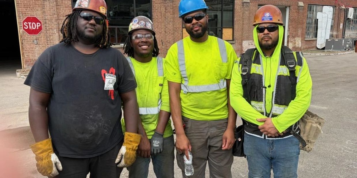 Four construction workers wearing safety gear pose together outdoors.