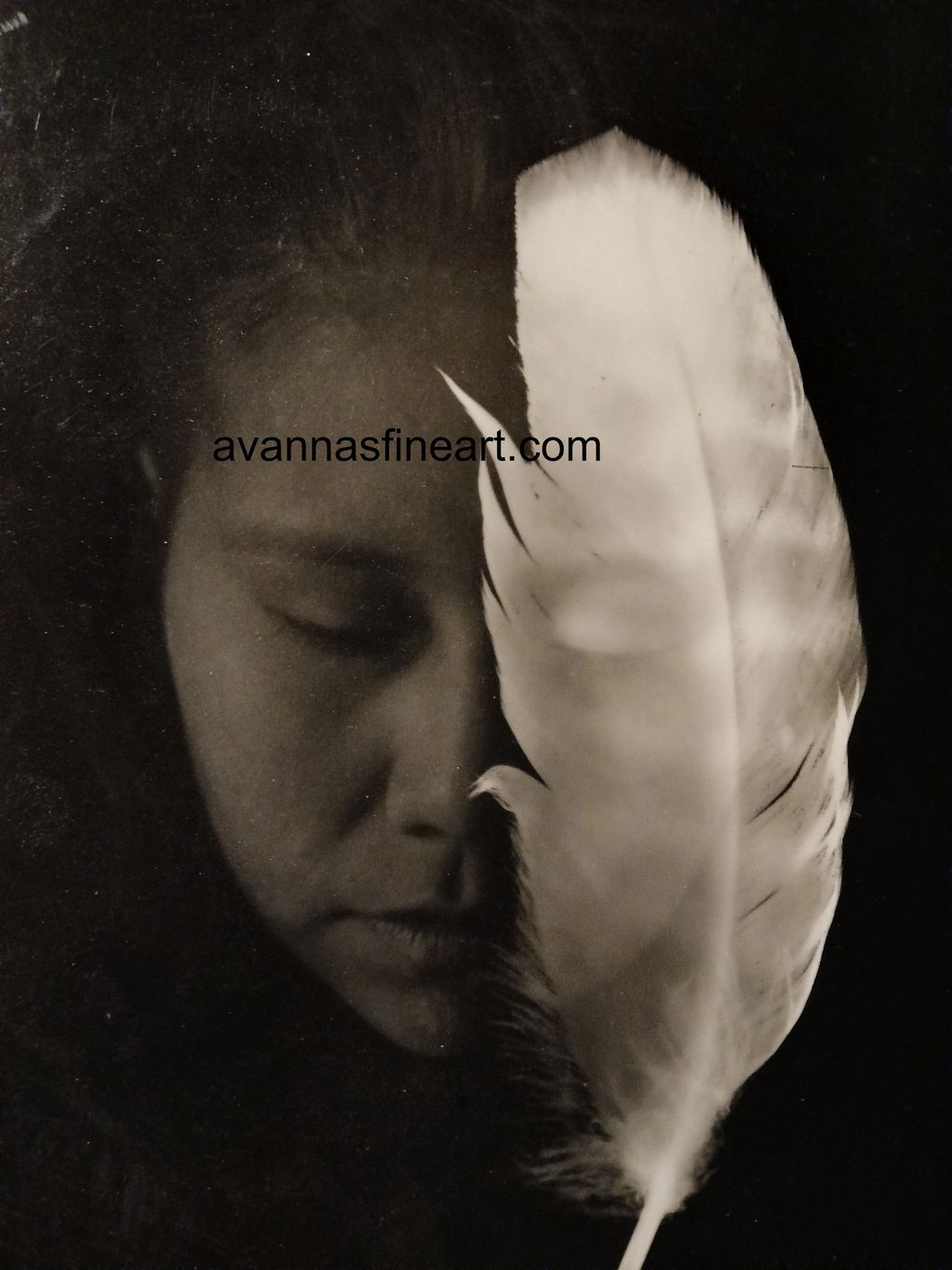 Black and white portrait of a woman holding a large feather close to her face.