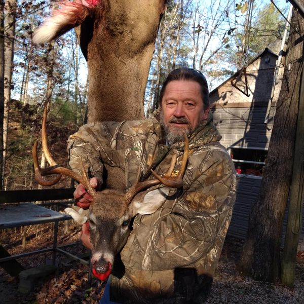 Hunter holding a large buck deer with antlers in a wooded area.