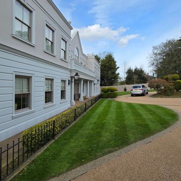 Elegant white building with manicured lawn and parked car on driveway.