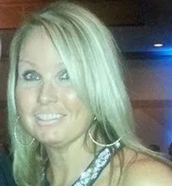 Smiling blonde woman with hoop earrings at an indoor event.