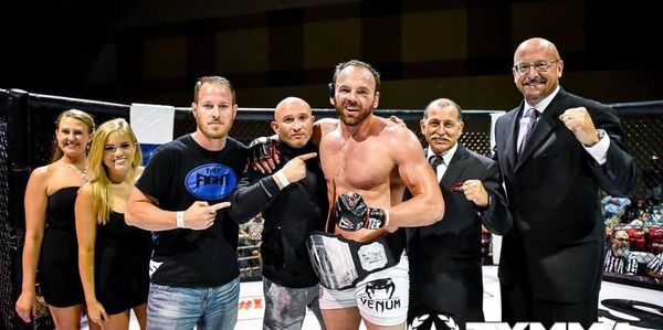 MMA fighter celebrates victory with team and officials inside the cage.
