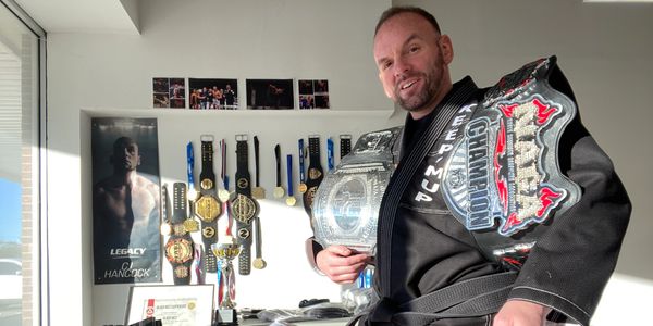 Man proudly displays multiple championship belts and medals in his room.