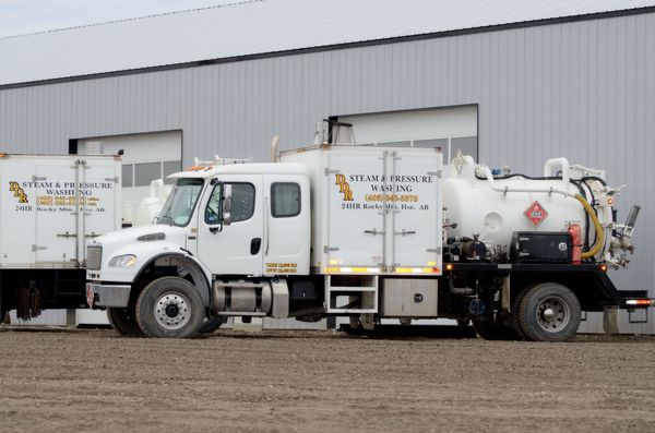 A white steam and pressure washing truck parked on a dirt lot, with company