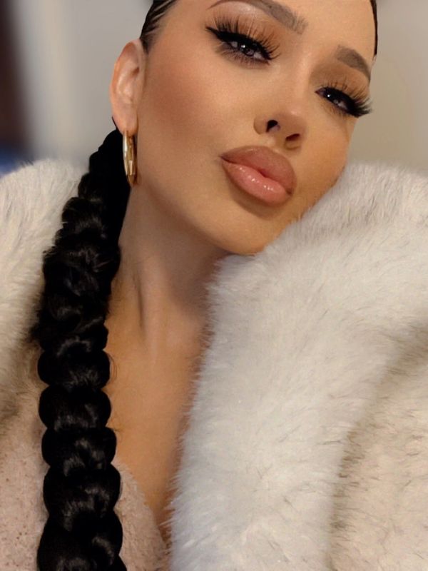 Woman with long braided hair and glamorous makeup wearing a white fur coat.