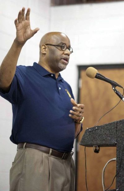 Man in navy polo shirt speaking at a podium with microphone.