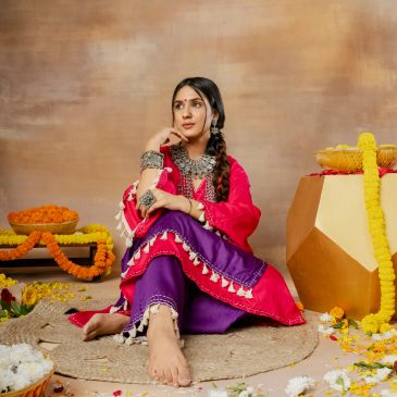 Woman in traditional attire sitting barefoot on a mat with flower decorations.