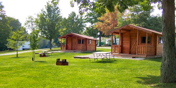 Two log cabins with picnic tables and fire rings in front.