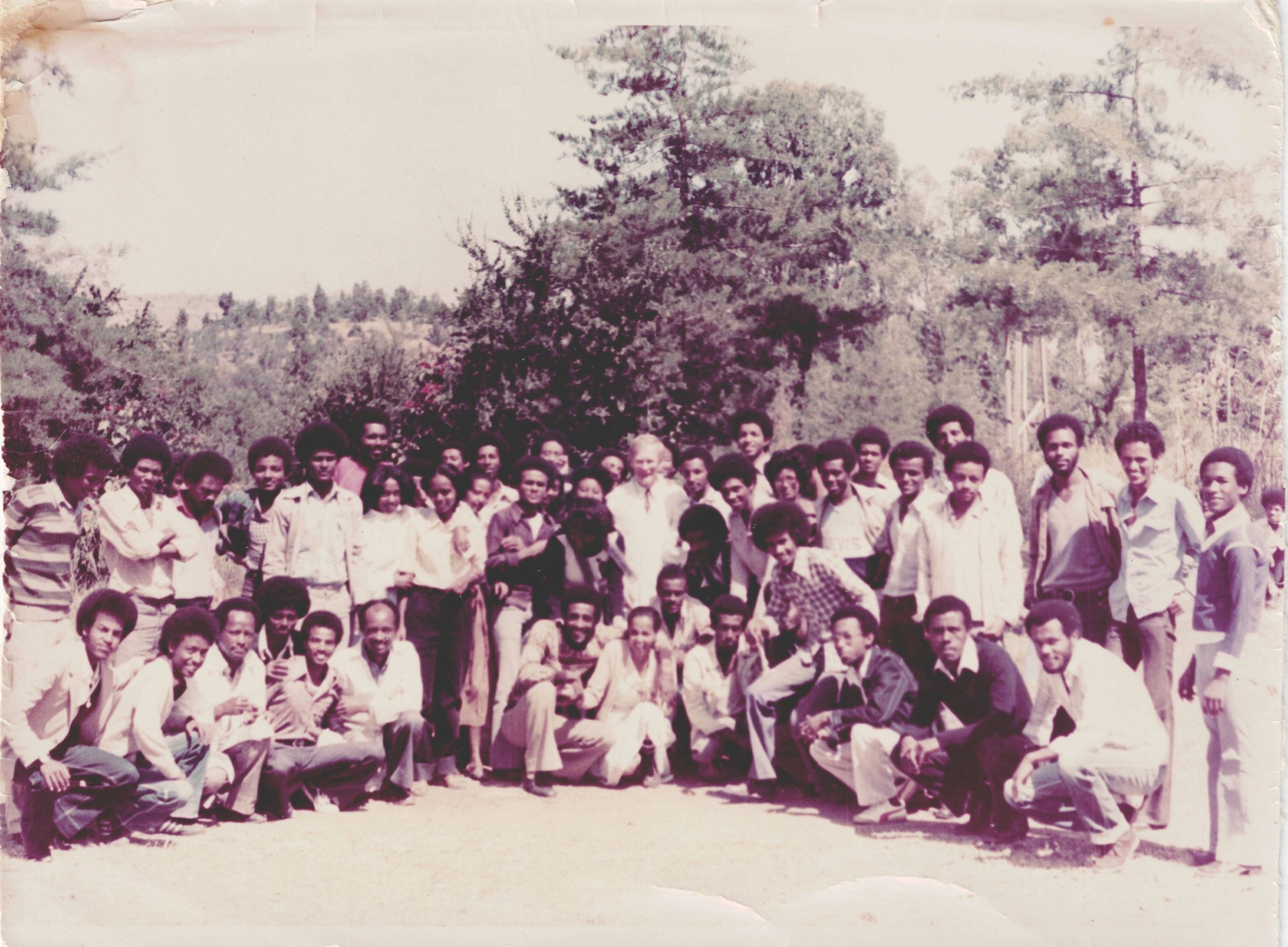 Large group of people posing outdoors in front of trees.