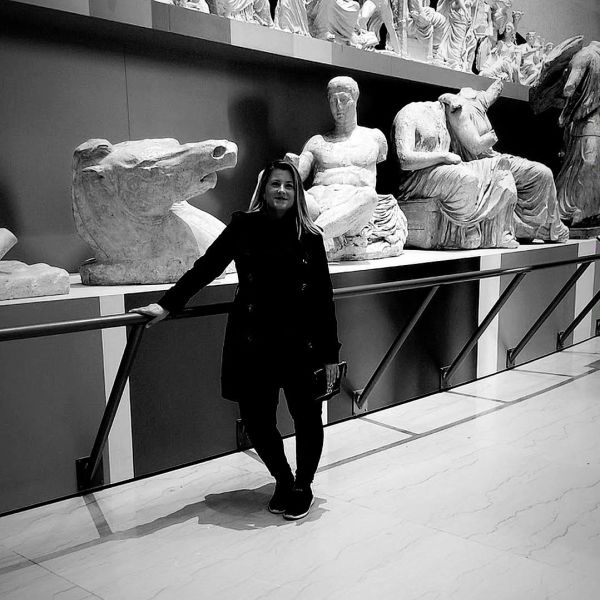 Woman posing with ancient sculptures in a museum.