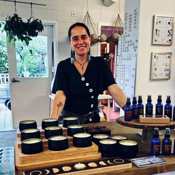 Sumayya smiles, standing behind a table full of her aromatherapy products. 