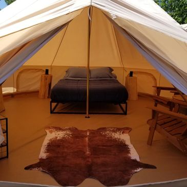 Inside view of a 5m bell tent, log side tables, cowhide rug, queen size bed, coffee table and chairs